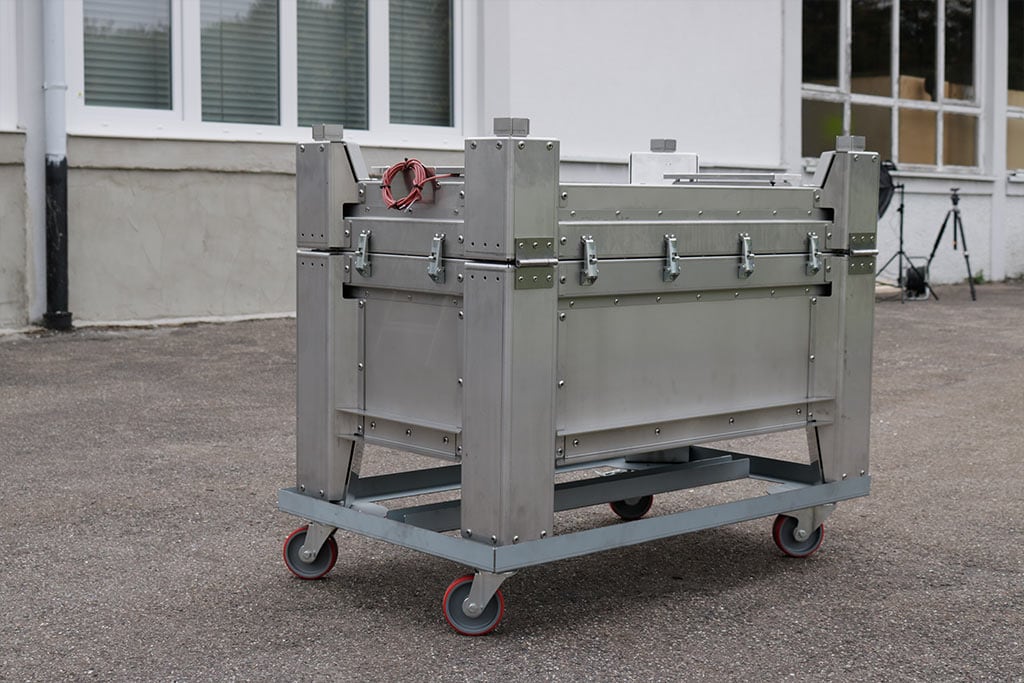 En sølvfarget metallbeholder på hjul foran en bygning.
