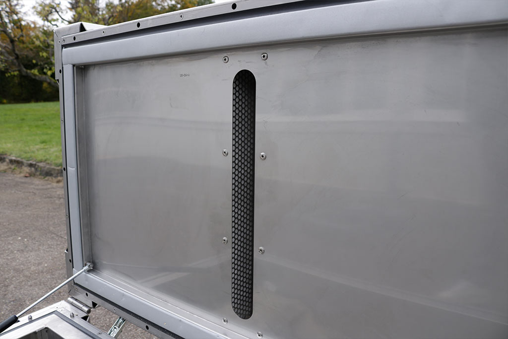 Metallpanel med et fintmasket, svart ventilasjonsgitter, omgitt av en sølvfarget ramme.