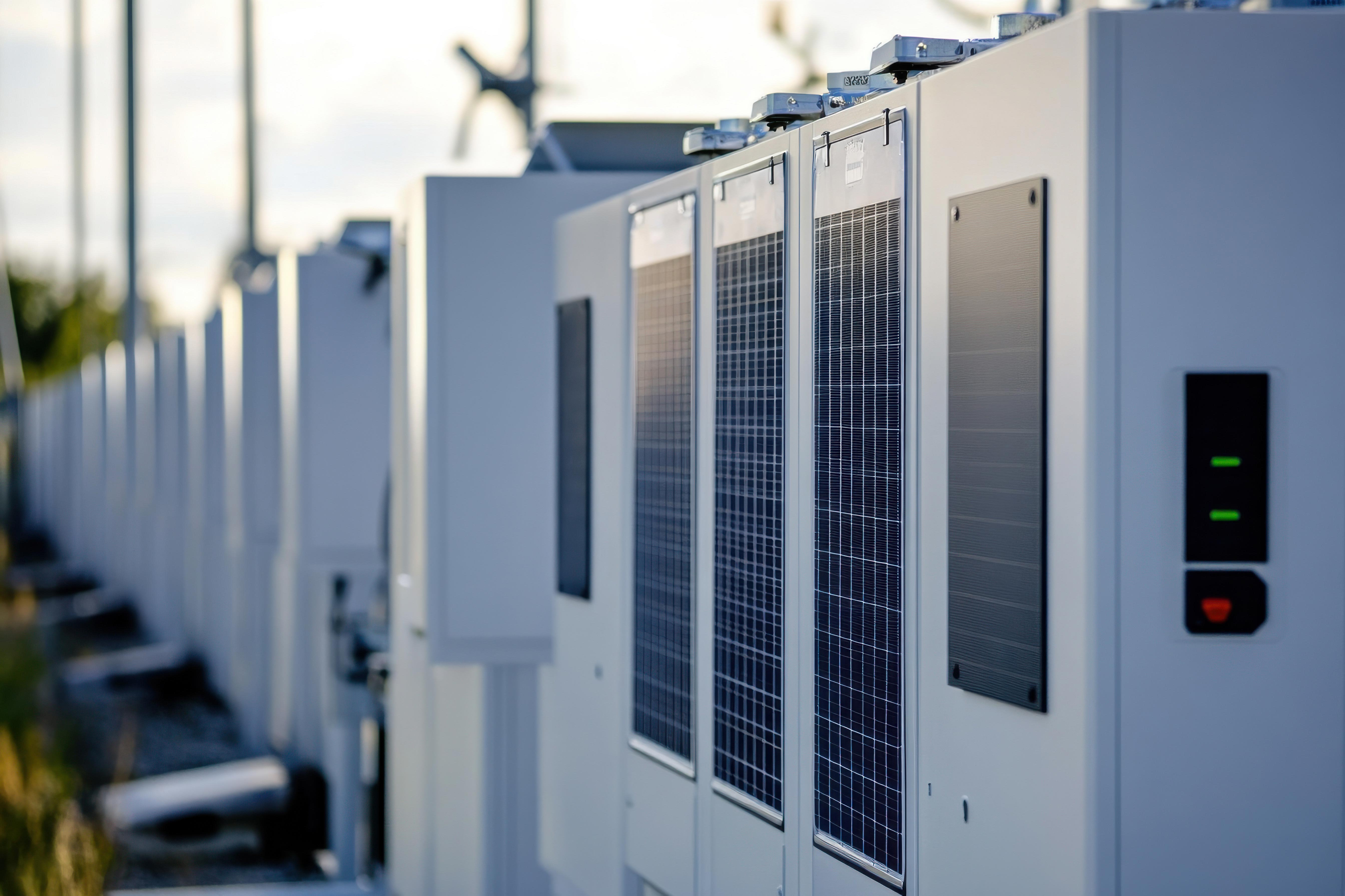 En rekke hvite batterilagringsenheter utendørs ved solnedgang; moderne energiinfrastruktur.